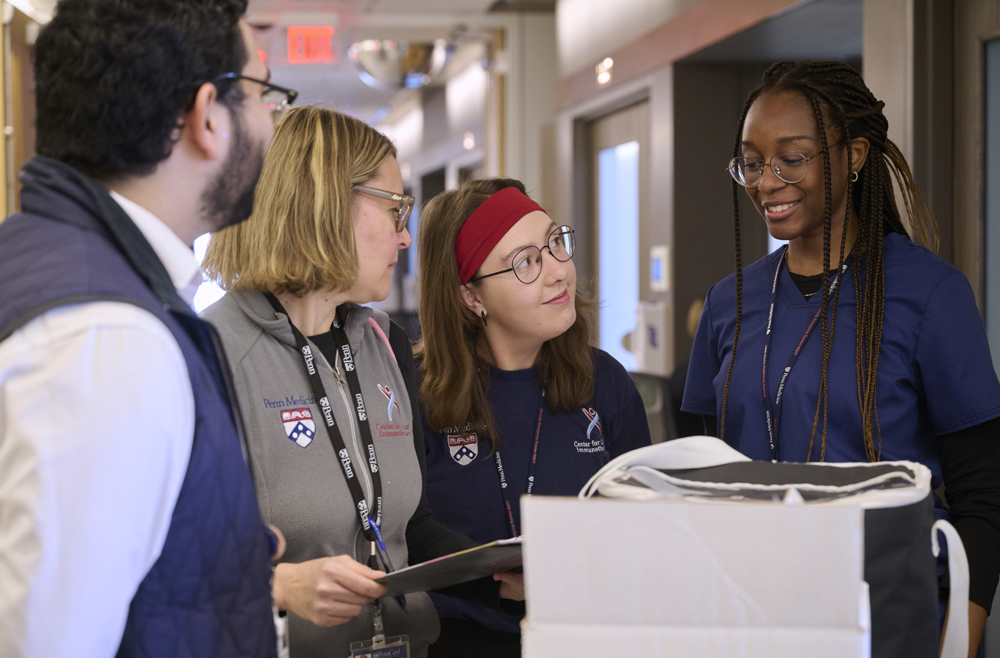 Four Clinical Research staff members have a conversation around a cart in a hospital hallway.